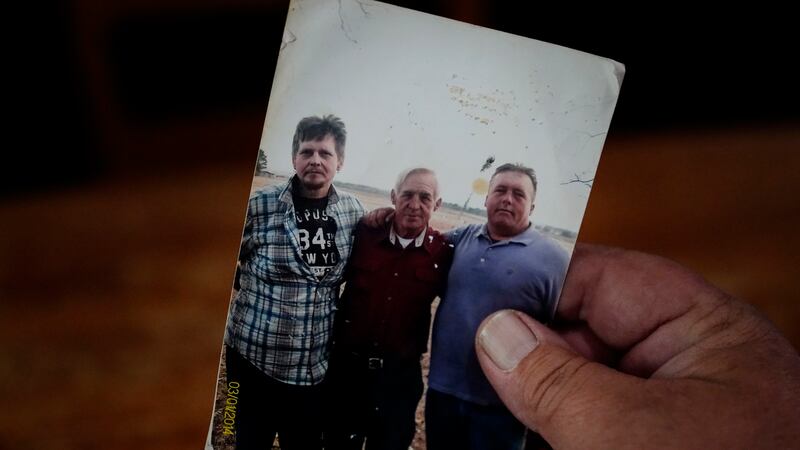 Daniel Guess holds a photograph of himself, right, along with his father, Larry Guess, center,...